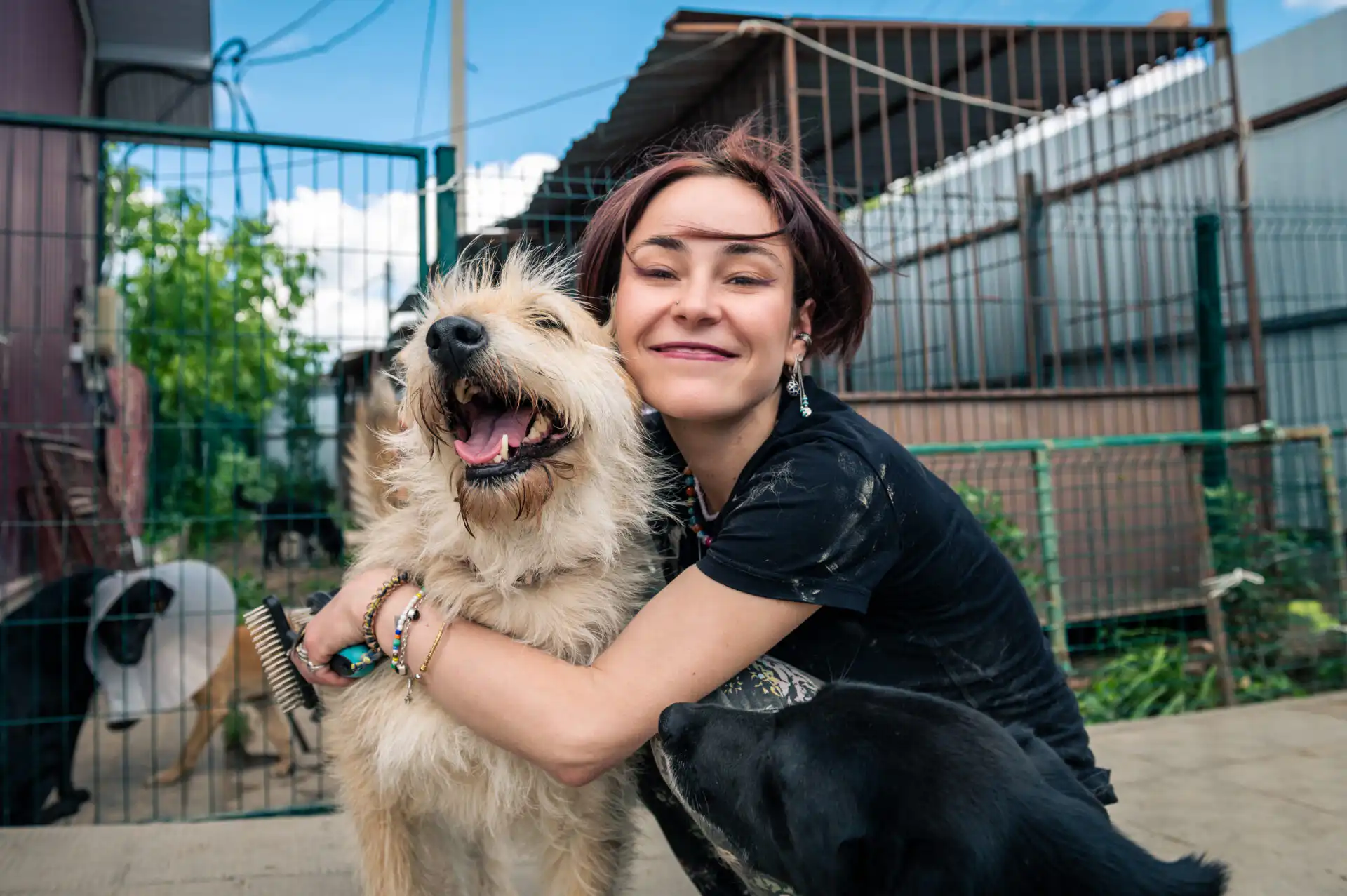 Woman hugging and gently holding a smiling mixed breed rescue dog inside a fenced outdoor rescue area